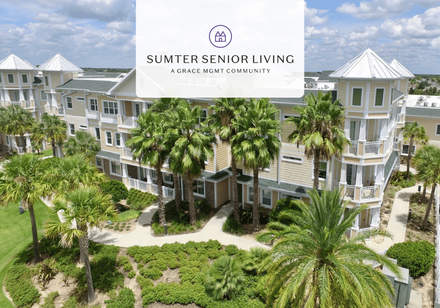 Aerial view of Sumter Senior Living campus with beige apartment buildings, palm trees, and landscaped courtyards.