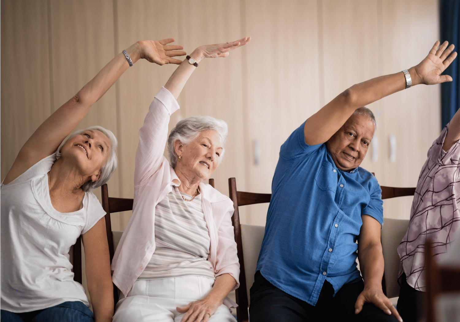 Group of seniors seated on chairs, raising their arms in a synchronized stretching exercise.